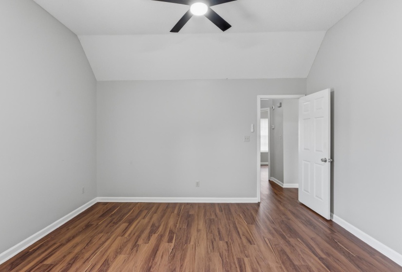 Vaulted ceiling room featuring wood-finish flooring, light gray wall paint, and white baseboards