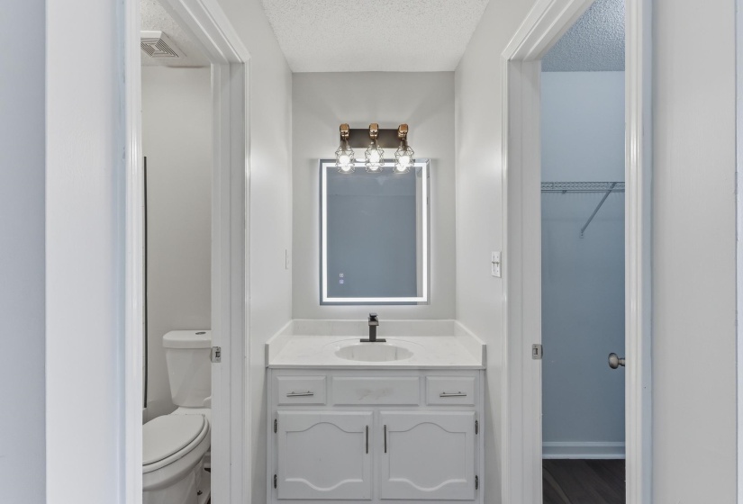 Vanity area featuring a quartz countertop, white cabinetry with silver-tone hardware, and a modern illuminated mirror