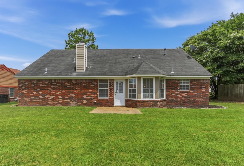 Expansive rear lawn featuring a brick exterior, a bay window, a concrete patio, and a chimney with vertical siding