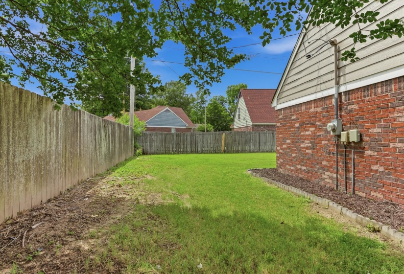 Expansive grassy yard area featuring a wooden privacy fence, brick exterior with beige siding, and mature tree canopy overhead