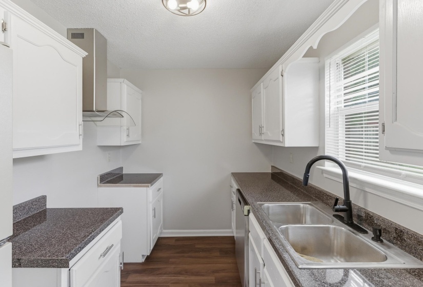 Galley kitchen featuring white cabinetry, dark speckled countertops, stainless steel dual basin sink with a matte black faucet, and wood-finish flooring