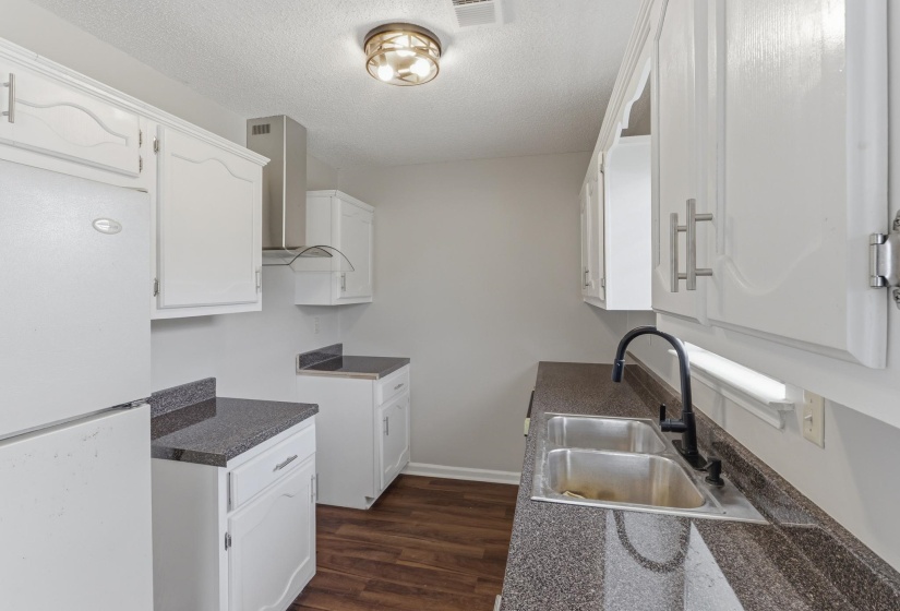 Kitchen featuring white cabinetry, dark speckled countertops, and wood-finish flooring