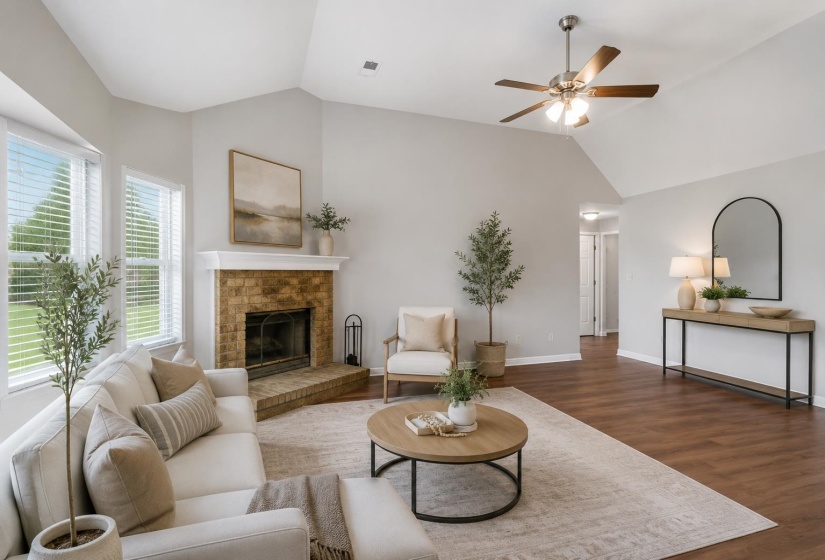 Spacious living room featuring a brick fireplace with a white mantel, vaulted ceilings, large windows with blinds, wood-finish flooring, and a ceiling fan