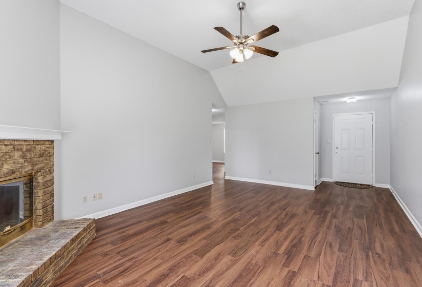 Spacious living area featuring wood-finish flooring, a brick fireplace with hearth, and vaulted ceilings