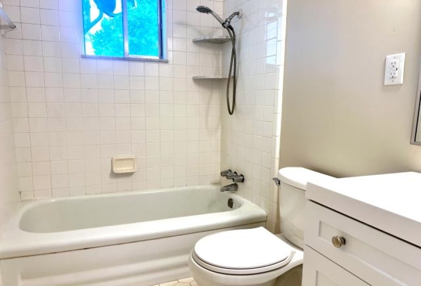 Bathroom featuring a white bathtub with subway tile surround, chrome fixtures, and a window