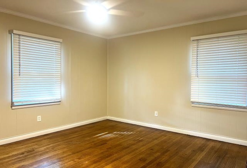 Spacious room featuring wood-finish flooring, two windows with blinds, crown molding, and a flush mount ceiling fixture