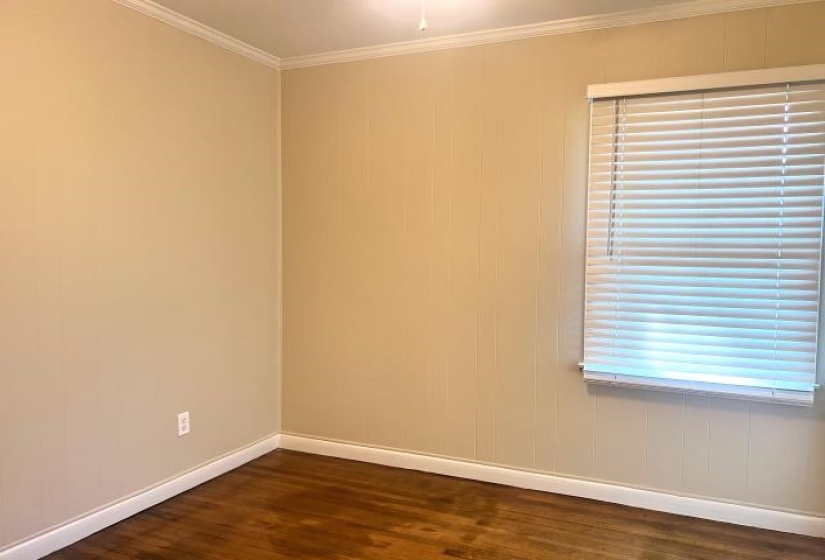 Interior space featuring hardwood flooring, light-colored walls, white baseboards, crown molding, and a window with horizontal blinds