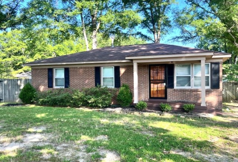 Brick single-story residence featuring a covered front porch, dark shutters, and a wood security storm door