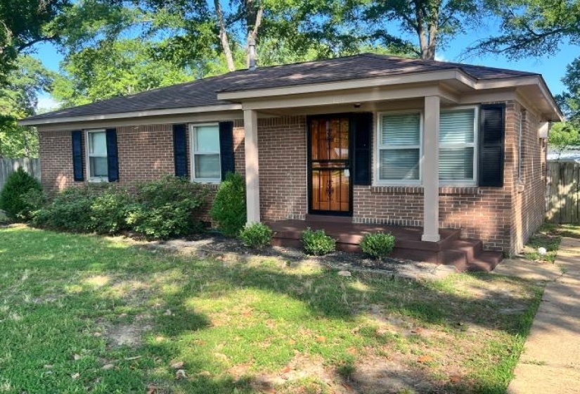 Brick exterior with dark shutters, covered front porch, and mature landscaping