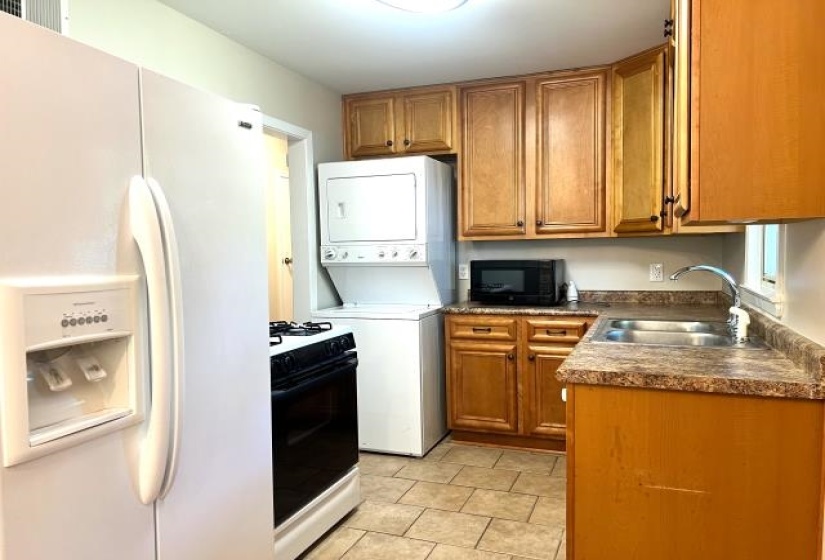 Kitchen featuring wood cabinetry, a stainless steel sink, tiled flooring, and a stacked washer and dryer unit