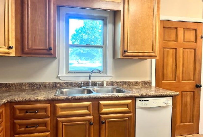 Kitchen featuring wood cabinetry, a double-basin stainless steel sink with a chrome faucet, and a white built-in dishwasher