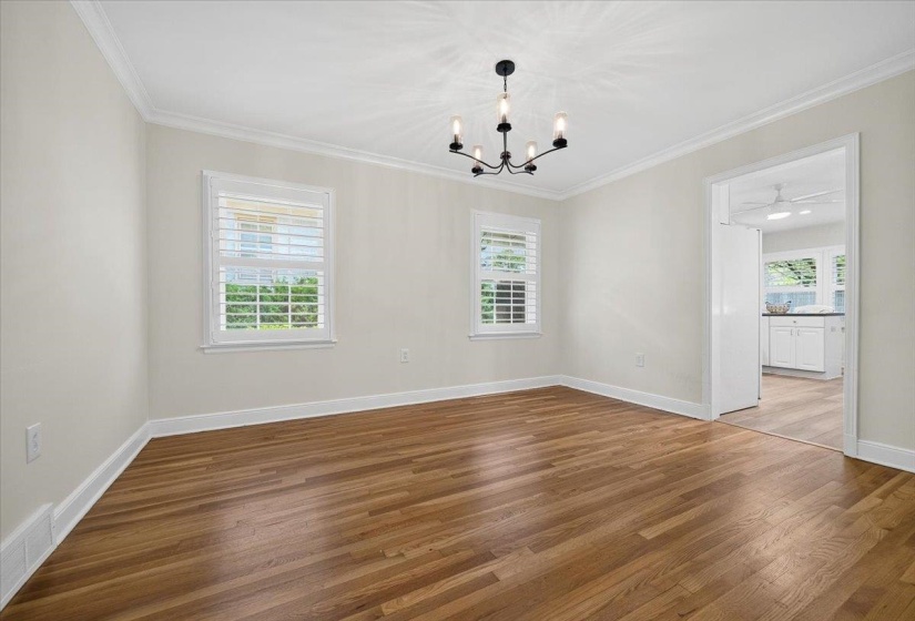 Spacious room featuring wood-finish flooring, two windows with white plantation shutters, crown molding, and a modern black chandelier