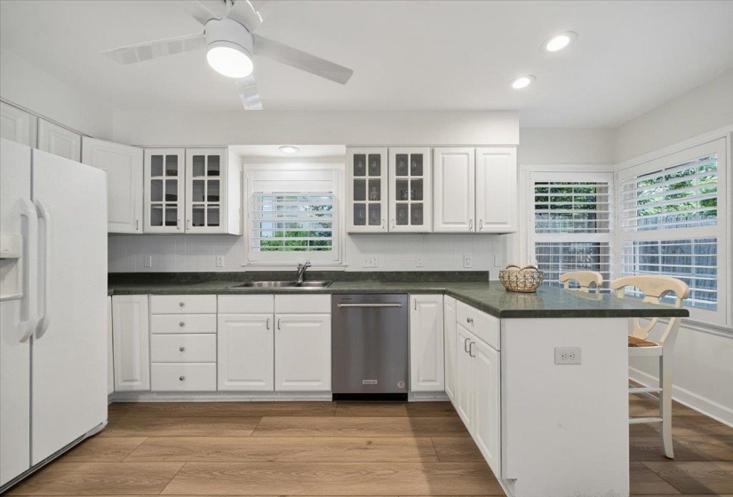 Well-appointed kitchen featuring extensive white cabinetry, a built-in stainless steel dishwasher, a single-basin sink, and wood-finish flooring