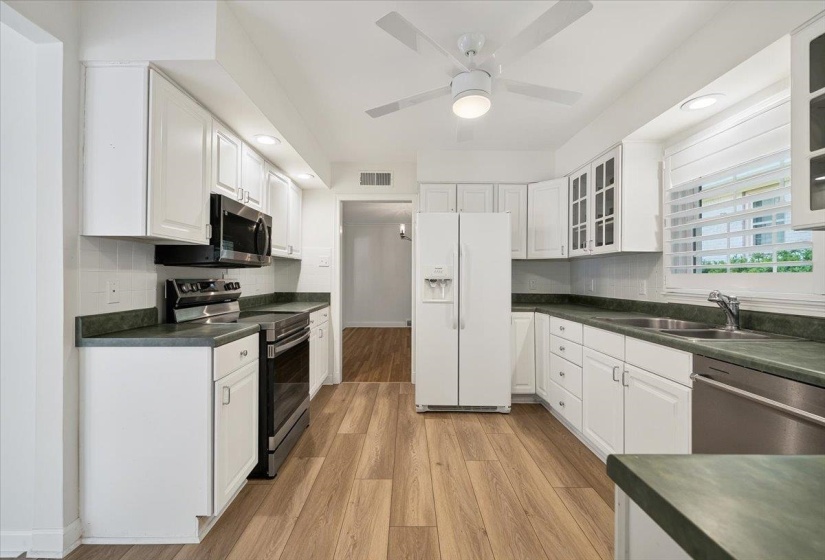 Kitchen featuring white cabinetry, dark countertops, wood-finish flooring, stainless steel dishwasher, and a white appliance package