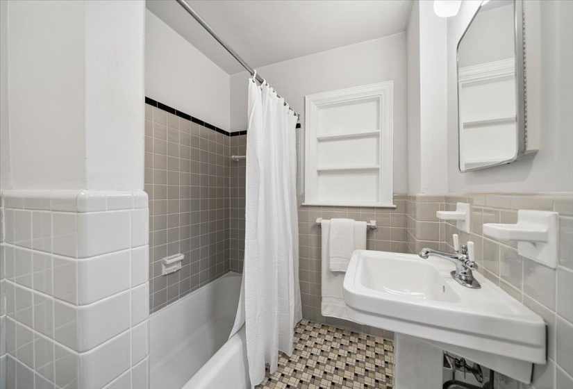 Bathroom featuring a pedestal sink, mosaic tile flooring, and a subway-tiled shower surround