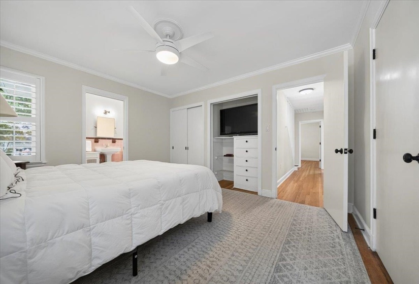 Spacious bedroom featuring crown molding, a ceiling fan with integrated lighting, wood-finish flooring, and built-in shelving with drawers