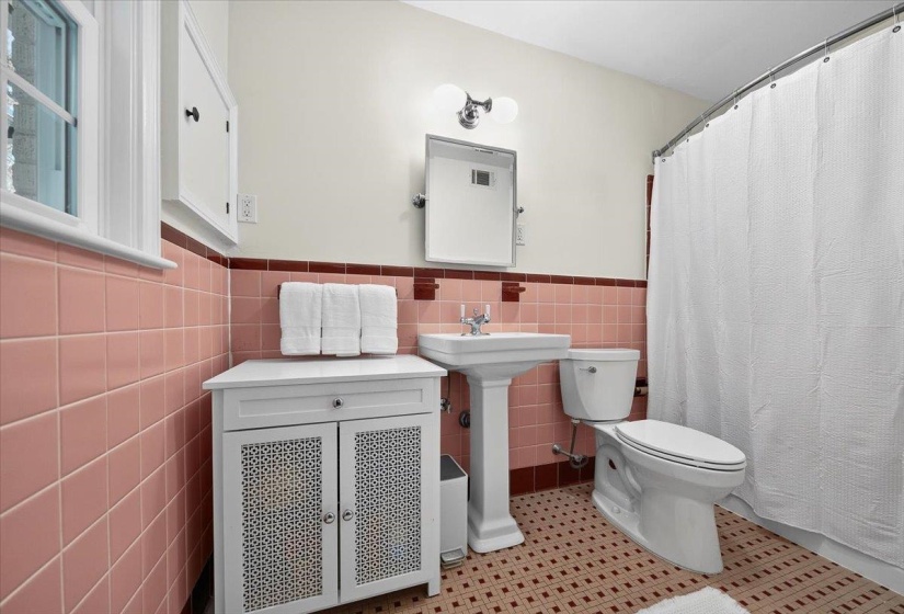 Bathroom featuring pink wall tiling, a pedestal sink, white toilet, and a shower with a white curtain