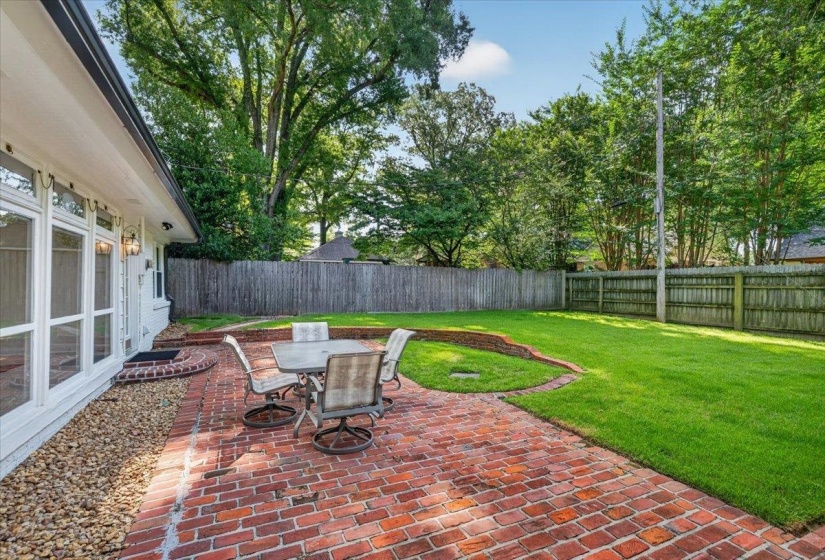 Expansive backyard featuring a red brick paver patio, manicured lawn, and perimeter wood fencing