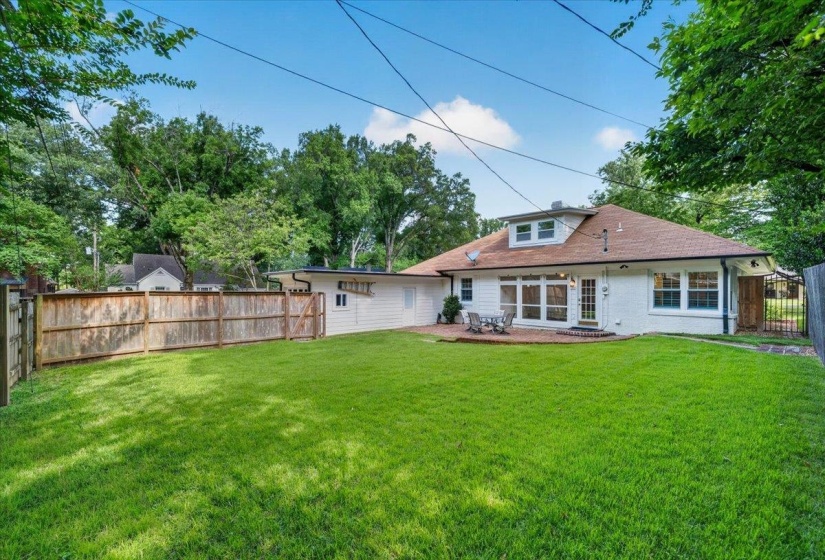 Spacious backyard featuring a large grass area, wood privacy fencing, and a brick patio