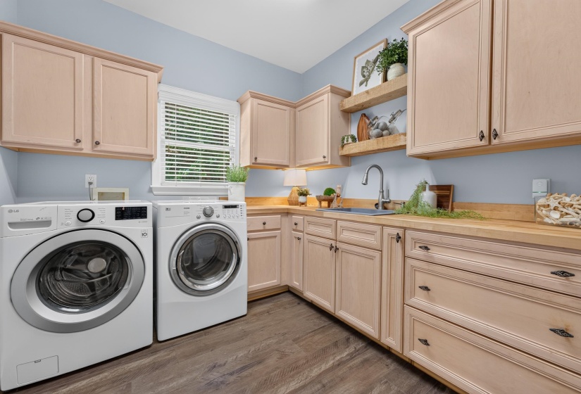 Laundry area featuring wood-finish flooring, ample cabinetry, wood countertops, a stainless steel sink with a gooseneck faucet, and a window with blinds