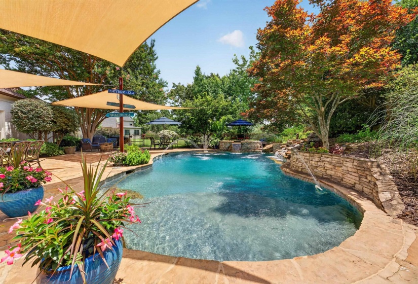 Curved swimming pool with stone waterfall features and surrounding hardscaping