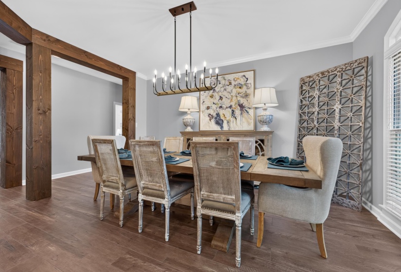 Open-concept dining area featuring wood-finish flooring, a contemporary chandelier, and an archway with exposed wood beams