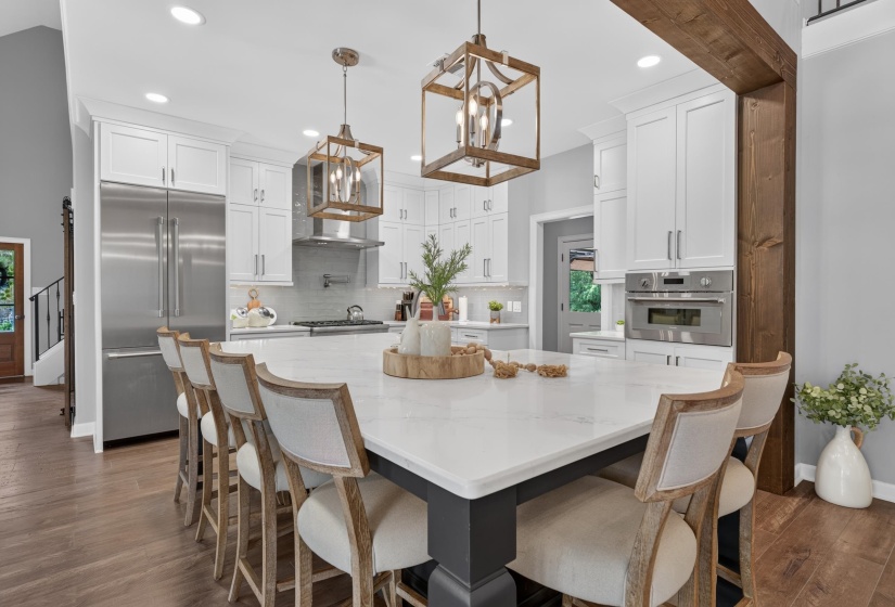 Spacious kitchen featuring a large central island with seating, white shaker cabinetry, stainless steel appliances, and wood-finish flooring