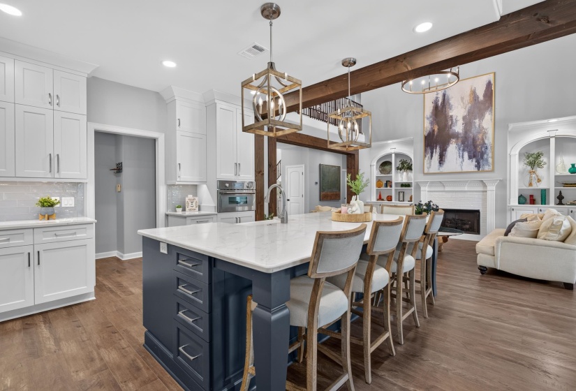 Open-concept kitchen featuring a spacious island with seating for four, white shaker cabinetry, light-toned subway tile backsplash, and wood-finish flooring