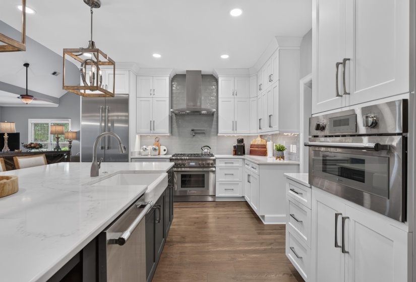 Contemporary kitchen featuring white cabinetry, stainless steel appliances, a large center island with a farmhouse sink, wood-finish flooring, and recessed lighting