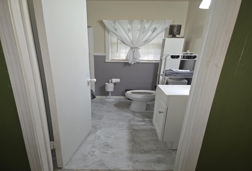 Bathroom featuring a white vanity with integrated sink, toilet, and a window with blinds