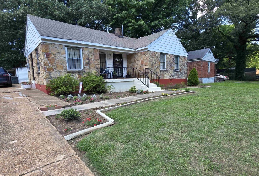 Stone facade home featuring a front porch with wrought iron railing, concrete drive, and established landscaping