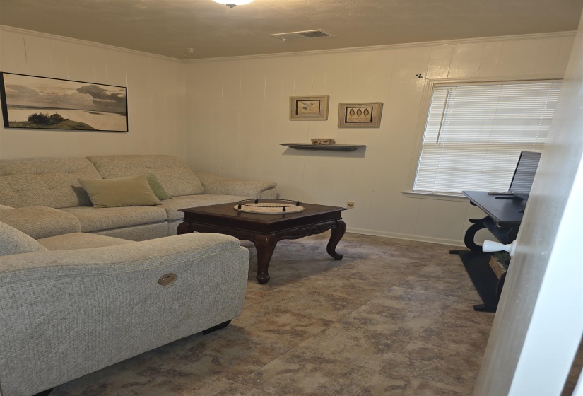 Living space featuring paneling on walls with crown molding, a window with blinds, and patterned tile-look flooring
