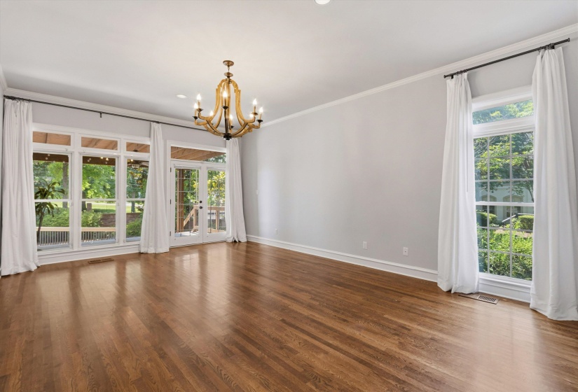 Spacious room featuring hardwood flooring, multiple large windows, and a classic chandelier