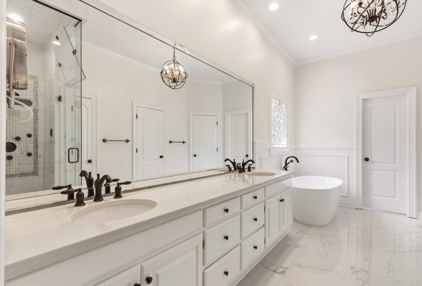 Spacious bathroom featuring a double vanity with stone countertop, freestanding soaking tub, frameless glass shower enclosure, and decorative ceiling light fixtures