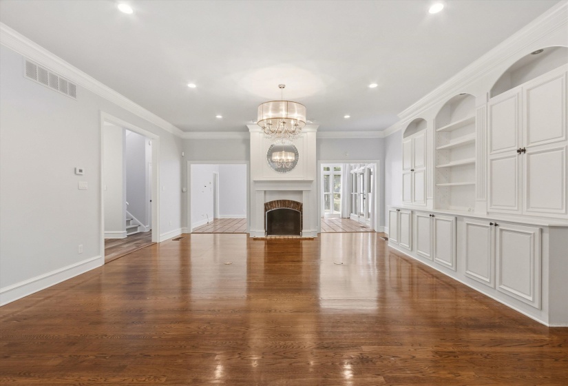Spacious interior featuring wood-finish flooring, a central fireplace with a white mantel, built-in cabinetry with arched shelving, recessed lighting, and a drum chandelier