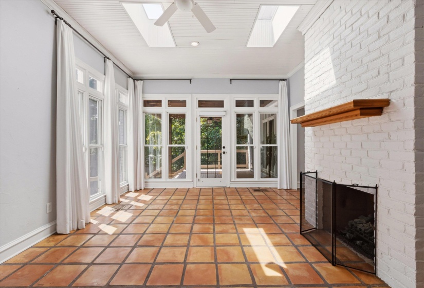 Spacious room featuring terra cotta tile flooring, a white-painted brick fireplace with a wood mantle, and a beadboard ceiling with skylights and a ceiling fan