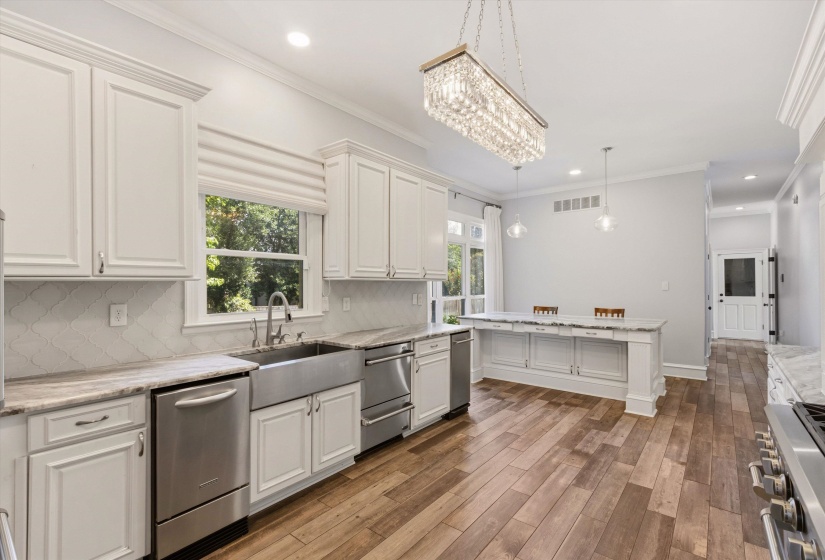 Gourmet kitchen featuring wood-finish flooring, white cabinetry, stainless steel appliances, a farmhouse sink, and a crystal chandelier