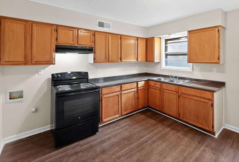 Kitchen featuring black / electric stove, dark countertops, brown cabinetry, dark wood finished floors, and under cabinet range hood