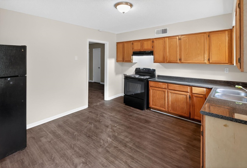 Kitchen featuring dark countertops, black appliances, dark wood-type flooring, brown cabinets, and under cabinet range hood