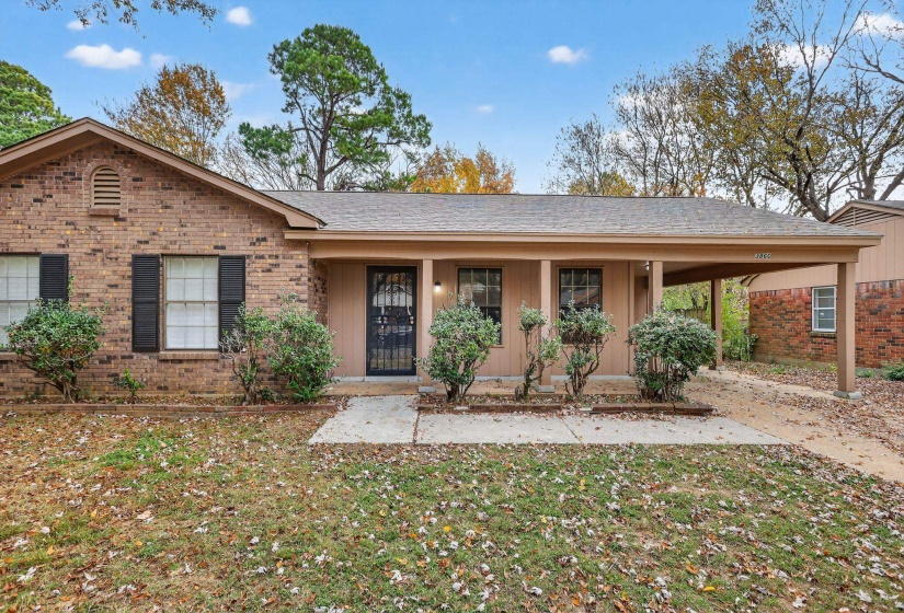 Ranch-style home with covered porch, brick siding, a carport, a front yard, and a shingled roof