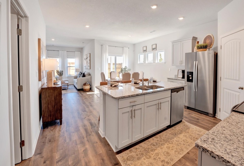 Kitchen with stainless steel appliances, light stone countertops, light wood-type flooring, a center island with sink, and open floor plan