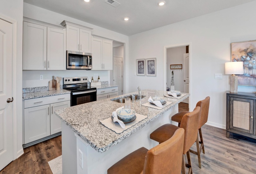 Kitchen with appliances with stainless steel finishes, light stone countertops, white cabinetry, a breakfast bar, and a center island with sink