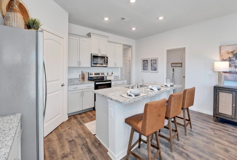 Kitchen featuring stainless steel appliances, a kitchen bar, dark wood-style floors, a kitchen island with sink, and light stone countertops