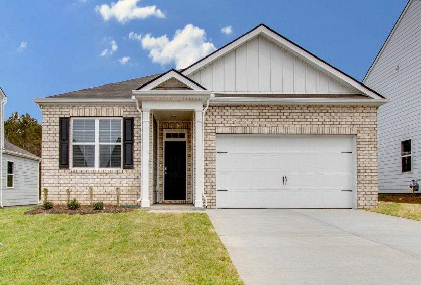 View of front of property with brick siding, board and batten siding, an attached garage, concrete driveway, and a front lawn