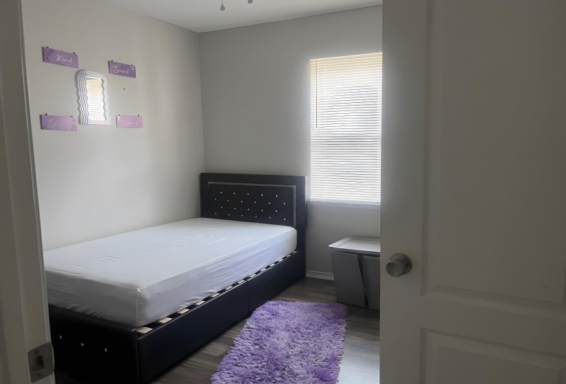 Bedroom featuring light gray walls, wood-finish flooring, and a single window with horizontal blinds