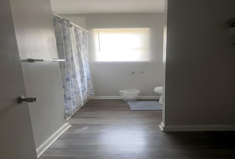 Bathroom featuring wood-finish flooring, a window with blinds, and white baseboards