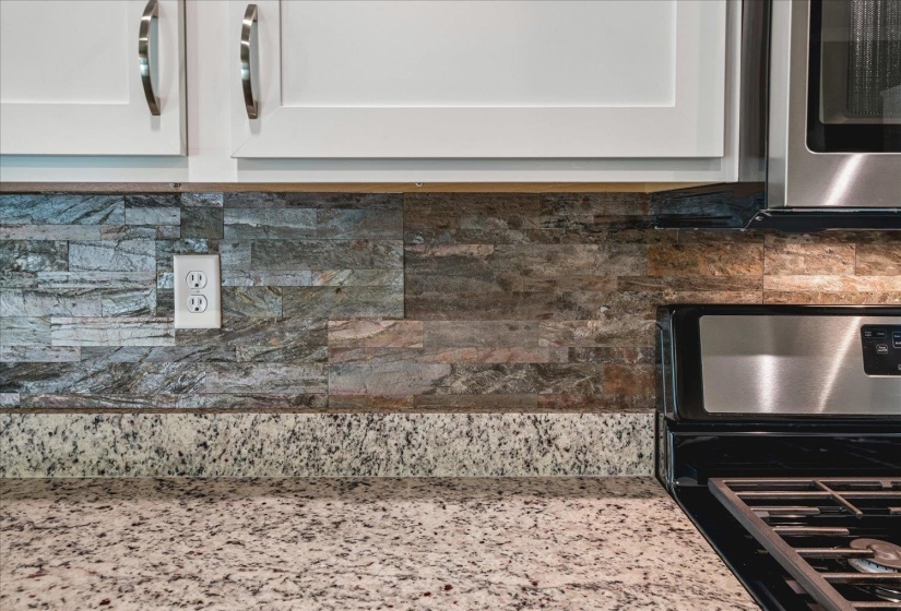 Kitchen featuring white cabinetry with brushed nickel hardware, a multi-tone stone tile backsplash, and a speckled countertop