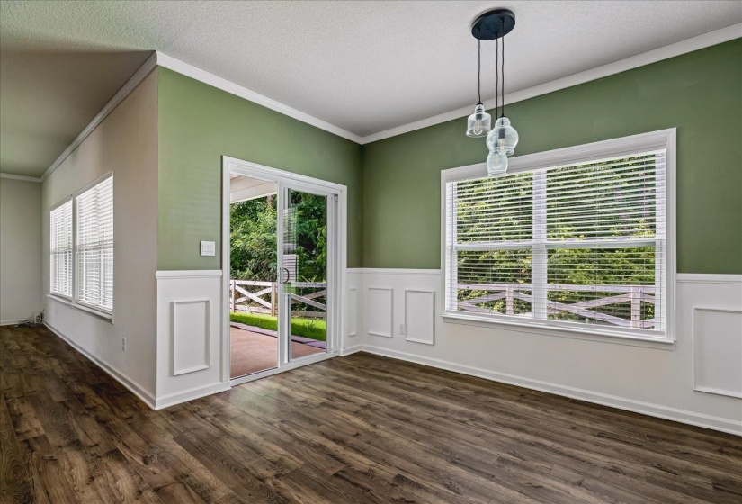 Spacious room featuring wood-finish flooring, wainscoting, and a multi-pane window with horizontal blinds