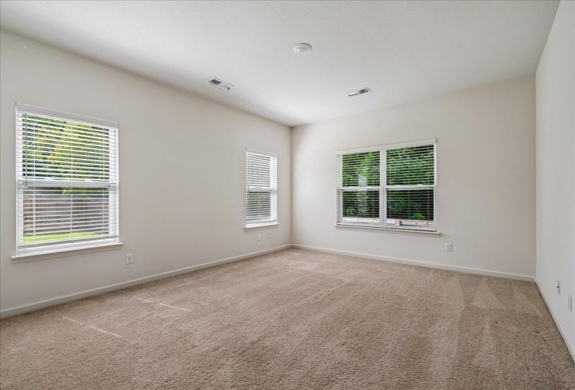 Spacious room featuring neutral carpeting, light-toned wall paint, and multiple windows with white blinds