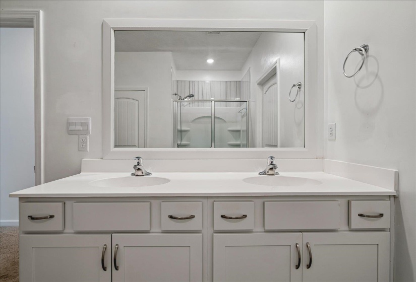 Double vanity featuring a white countertop with integrated sinks, chrome faucets, and white shaker-style cabinetry with curved handles